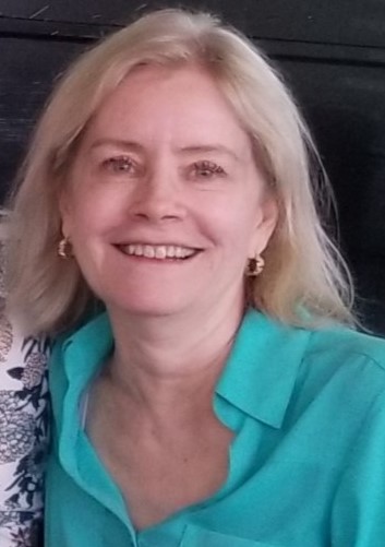 Smiling woman with blonde hair wearing a turquoise blouse, posing for a photo.
