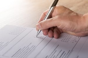 Close-up of a hand using a silver pen to fill in a checkbox on a form or survey.