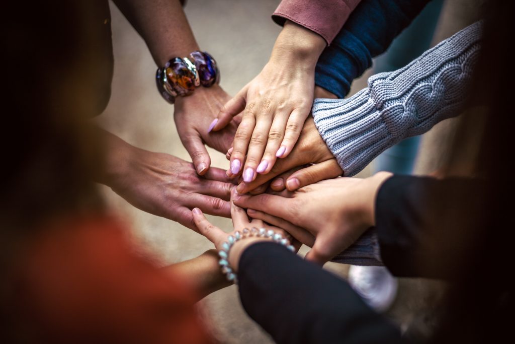 Several hands stacked on top of each other in a circle, symbolizing teamwork and collaboration in a diverse group.